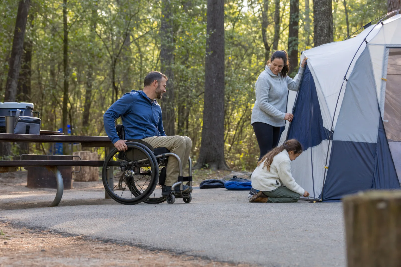 A wheelchair user and family members set up a tent on a level accessible campsite.