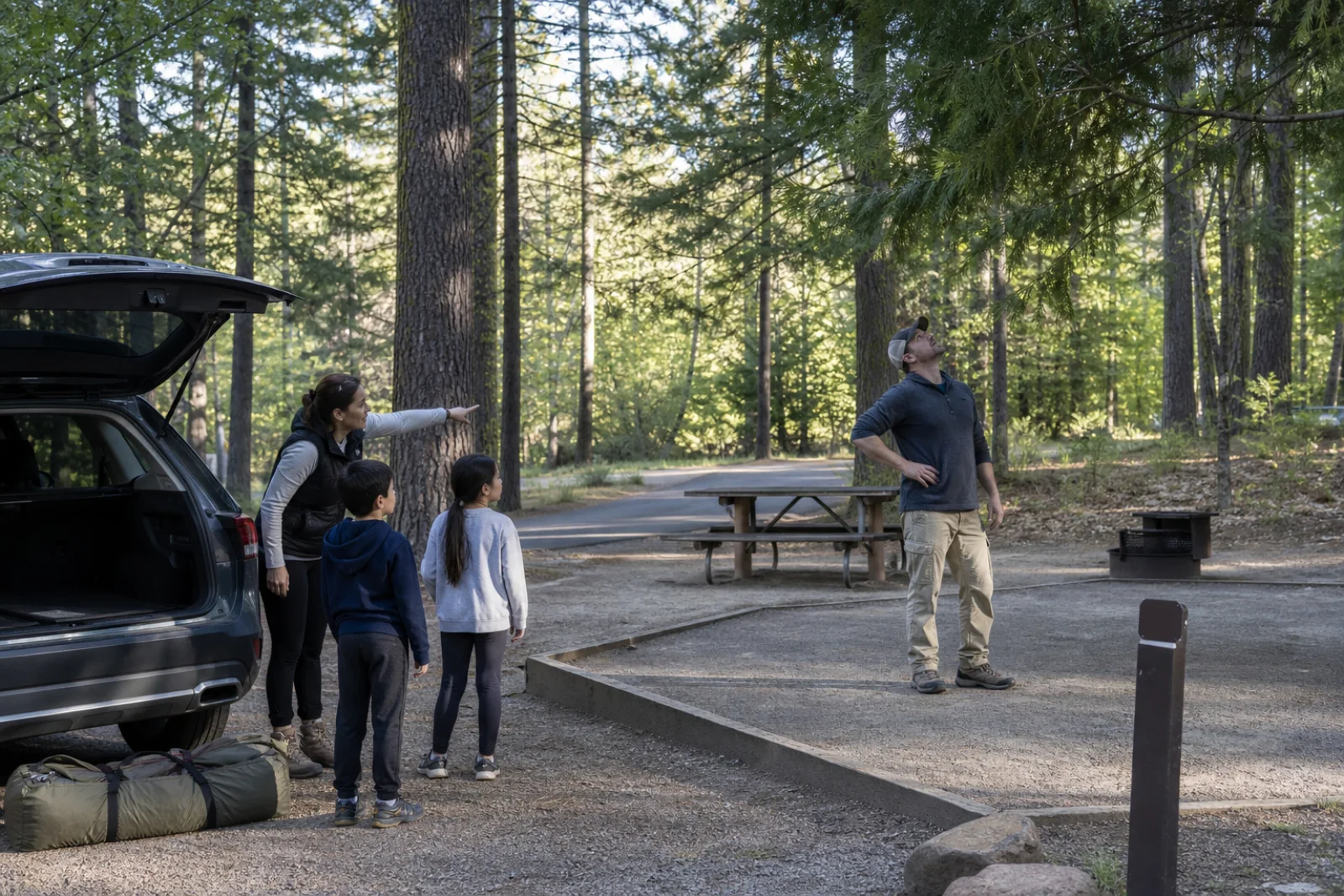 A family checks a developed forest campsite before unloading their car.